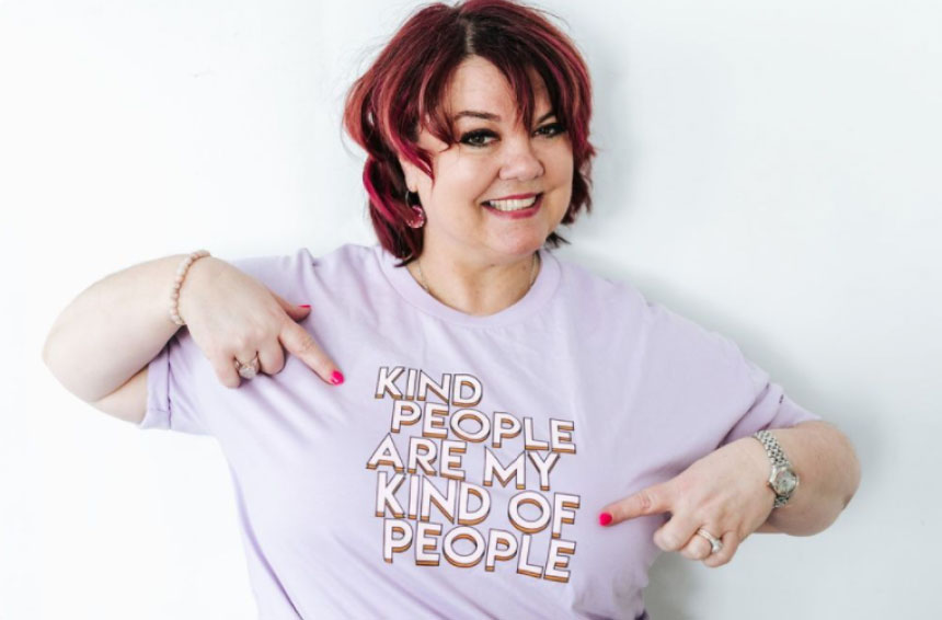 A smiling woman with red hair points to her lavender T-shirt that reads "Kind people are my kind of people." She has painted nails and wears a bracelet and watch, perfect for a social media scheduler post | plannthat.com