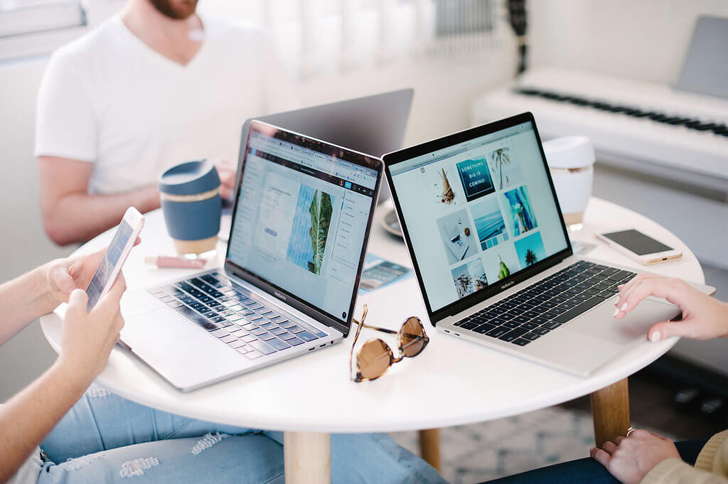 Three people working on laptops and smartphones at a round table with coffee cups and sunglasses in a bright room, using a social media scheduler | plannthat.com