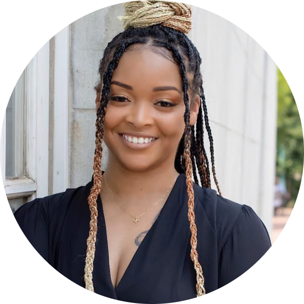 A woman with braided hair and a black top smiles, standing outdoors near a wall, showcasing her role as a social media planner | plannthat.com A woman with braided hair and a black top smiles, standing outdoors near a wall, showcasing her role as a social media planner | plannthat.com