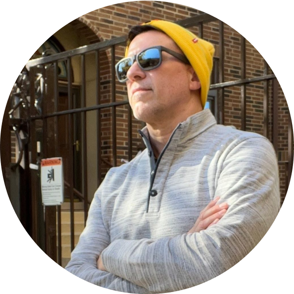 A man in a gray sweater and yellow beanie, wearing sunglasses, stands with arms crossed in front of a brick building with a gated entrance, looking confident and ready to use his social media scheduler | plannthat.com A man in a gray sweater and yellow beanie, wearing sunglasses, stands with arms crossed in front of a brick building with a gated entrance, looking confident and ready to use his social media scheduler | plannthat.com