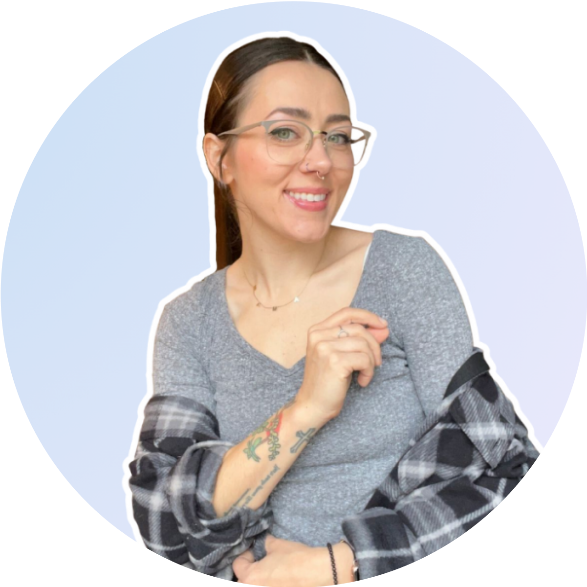 A woman wearing glasses and a grey top, with a plaid shirt draped over her shoulders, smiles against a light blue background. She has tattoos on her right arm and wears a necklace, embodying the creative spirit of a social media planner | plannthat.com A woman wearing glasses and a grey top, with a plaid shirt draped over her shoulders, smiles against a light blue background. She has tattoos on her right arm and wears a necklace, embodying the creative spirit of a social media planner | plannthat.com